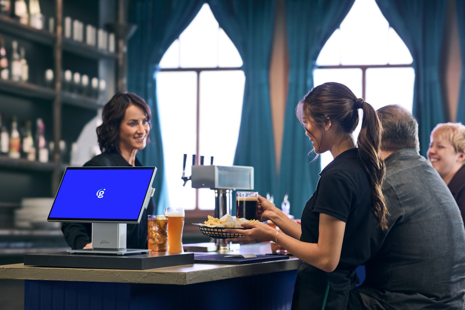 A server delivering food at a bar beside a Genius GC26 countertop POS terminal