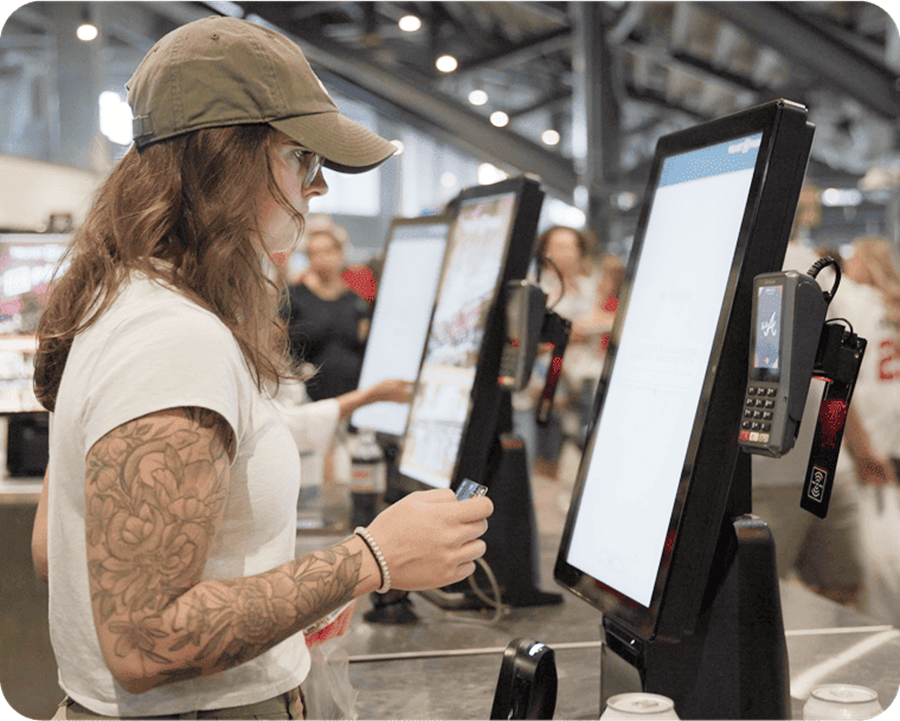 A guest ordering at a row of Genius self-order kiosks