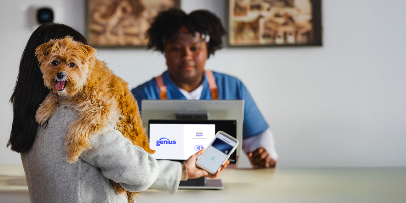 A shop owner holding a dog while taking a payment on a Genius device