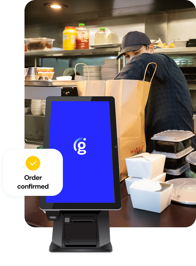 A busy kitchen scene with a team member bagging orders beside a self-ordering kiosk