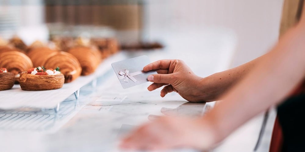 A gift card tied with a ribbon being handed across a bakery counter